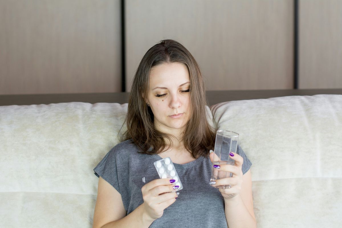A woman sitting on a couch, looking at her medication and a glass of water before a dose